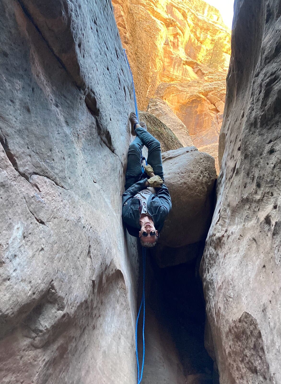A person hanging upside down on a blue rope between narrow sandstone walls