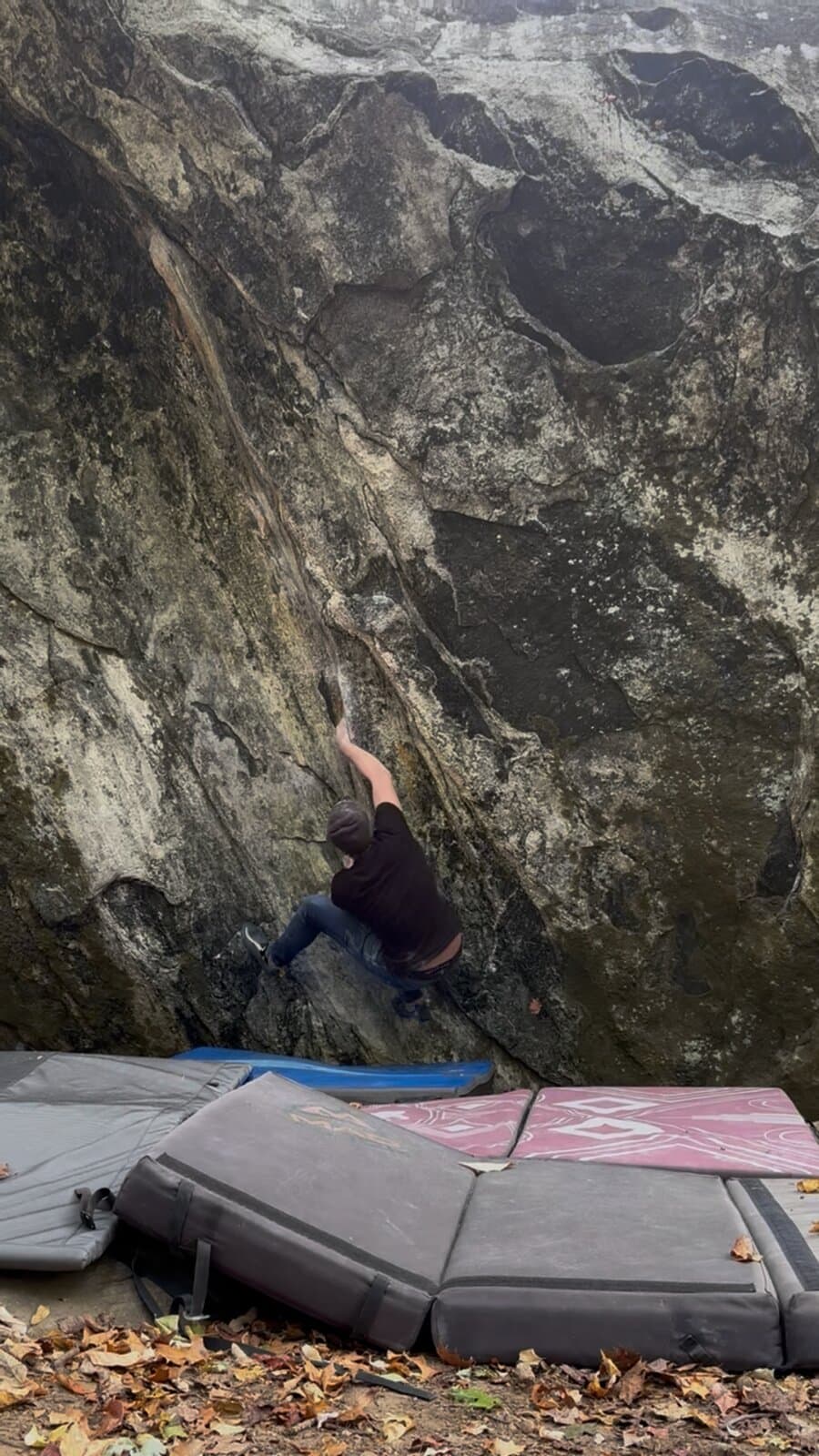 A climber reaching up a dark, overhanging boulder above crash pads