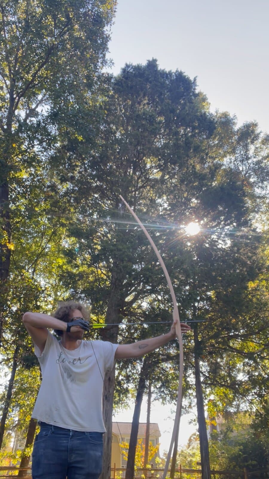 An archer at full draw with the longbow under tall trees