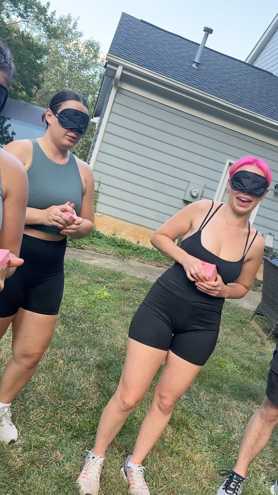 Two blindfolded contestants in a backyard, one laughing