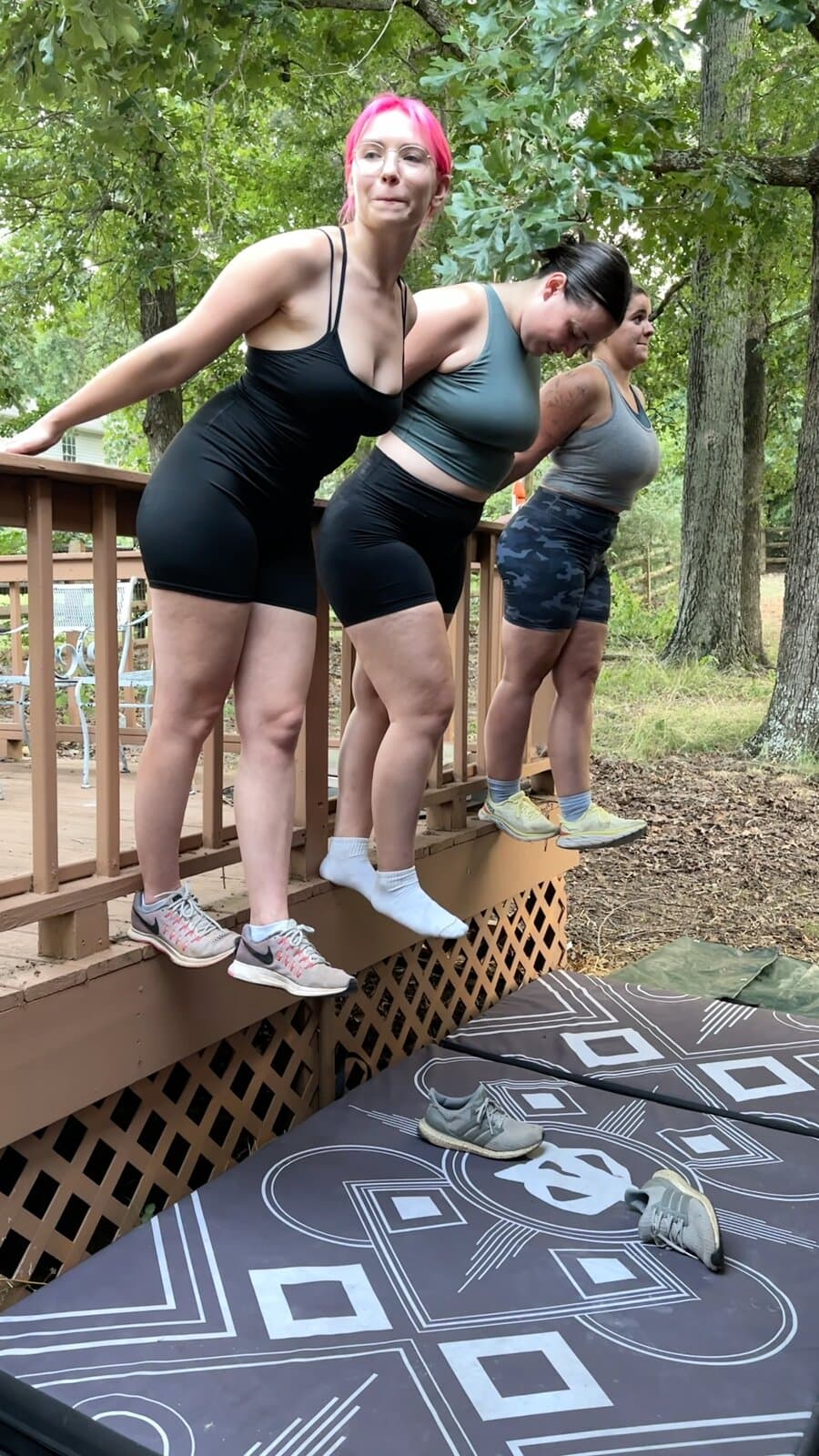 Three contestants leaning out over crash pads from the edge of a deck
