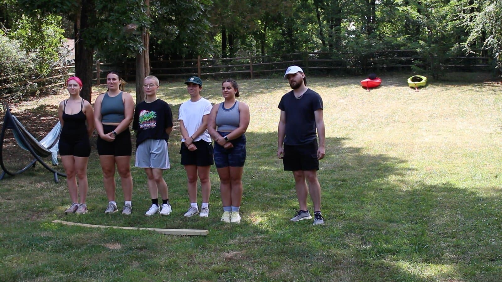 Six contestants standing in a line on a backyard lawn